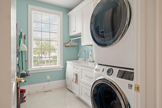 washroom with cabinet space, light tile patterned floors, baseboards, stacked washer / drying machine, and a sink