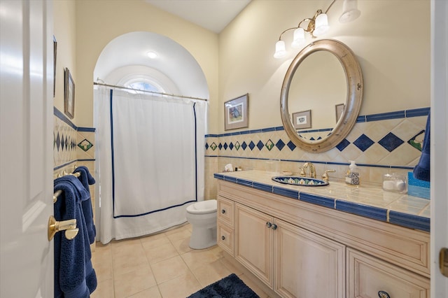 bathroom featuring a wainscoted wall, tile walls, toilet, vanity, and tile patterned flooring