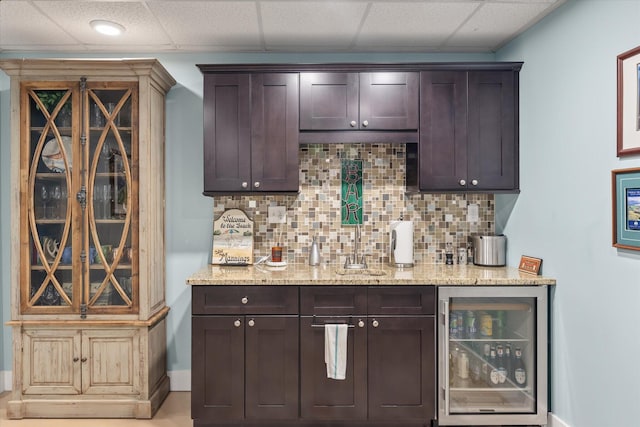 bar featuring beverage cooler, tasteful backsplash, a drop ceiling, a bar, and a sink