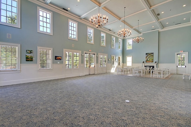 unfurnished living room with a notable chandelier, a wainscoted wall, carpet floors, coffered ceiling, and ornamental molding