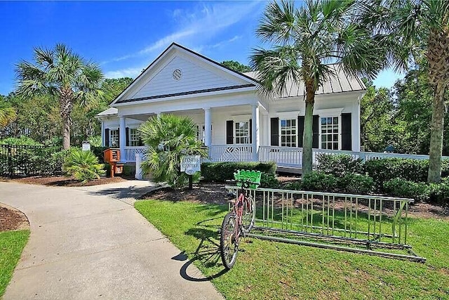 neoclassical home with concrete driveway, metal roof, fence, a porch, and a front yard