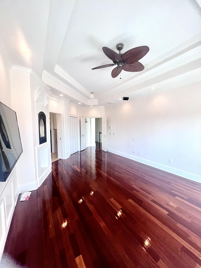 unfurnished living room with crown molding, a raised ceiling, a ceiling fan, wood finished floors, and baseboards