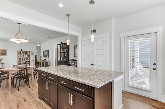 kitchen featuring pendant lighting, light wood-style flooring, light stone counters, a center island, and dark brown cabinetry