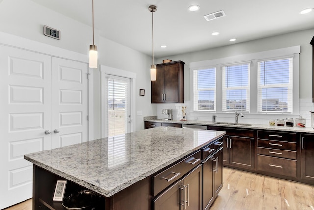 kitchen with a kitchen island, dark brown cabinetry, light stone counters, light wood-style flooring, and a sink