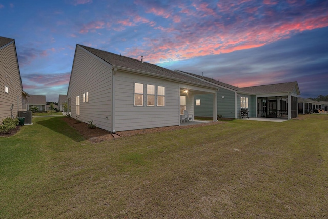 back of property at dusk with a yard, a patio area, cooling unit, and a sunroom