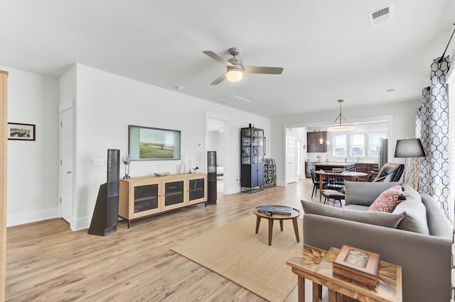 living room with a ceiling fan, visible vents, light wood finished floors, and baseboards