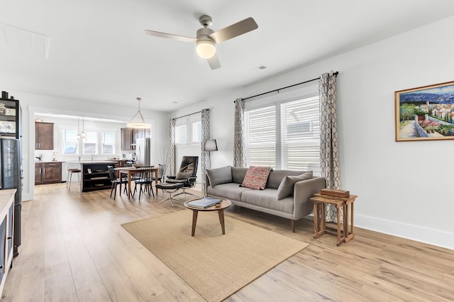 living area with visible vents, baseboards, beverage cooler, light wood-type flooring, and a ceiling fan