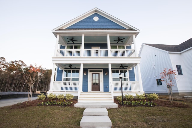 view of front facade with a front lawn, a balcony, a ceiling fan, and covered porch