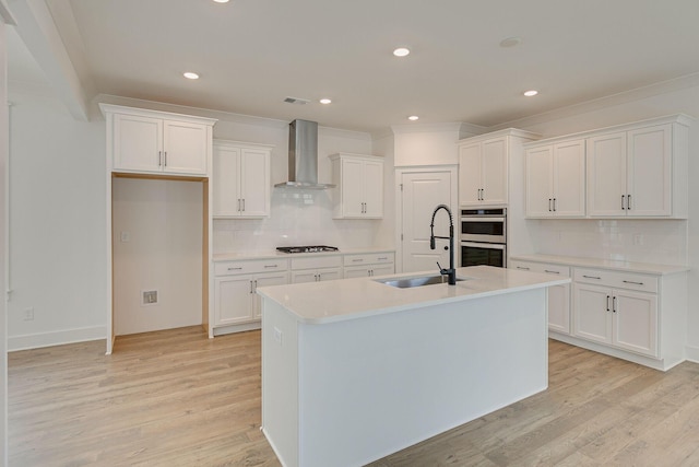 kitchen featuring light wood-style floors, stainless steel double oven, white cabinets, wall chimney exhaust hood, and a sink