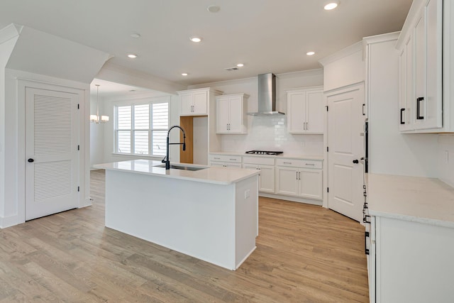 kitchen featuring a notable chandelier, light wood-style flooring, a sink, wall chimney exhaust hood, and white cabinets