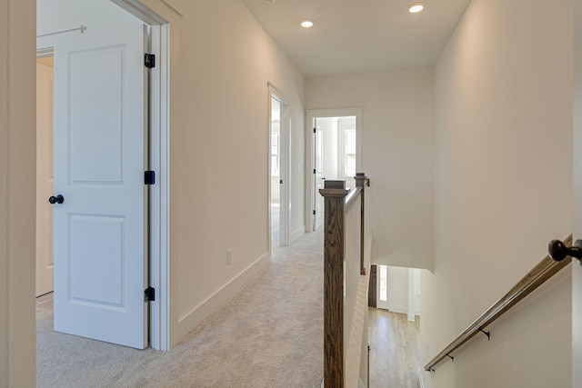 hall with an upstairs landing, recessed lighting, light colored carpet, and baseboards