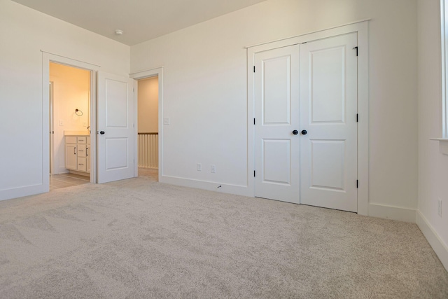 unfurnished bedroom with a closet, light colored carpet, ensuite bath, and baseboards