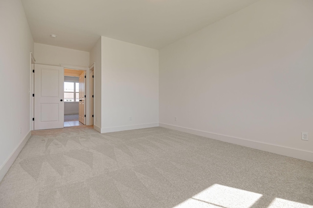 unfurnished room featuring light colored carpet and baseboards