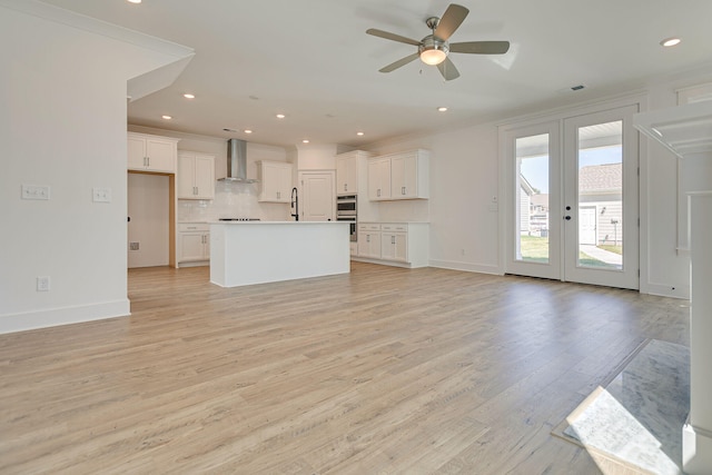 kitchen featuring a center island, wall chimney range hood, light wood-type flooring, and white cabinets