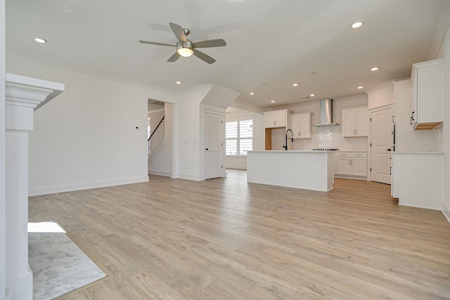 unfurnished living room featuring light wood-style flooring, stairs, crown molding, and a ceiling fan