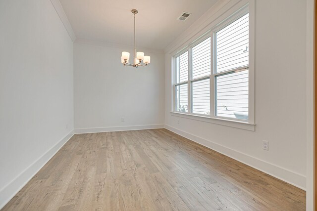 spare room featuring ornamental molding, light wood-style floors, baseboards, and a chandelier