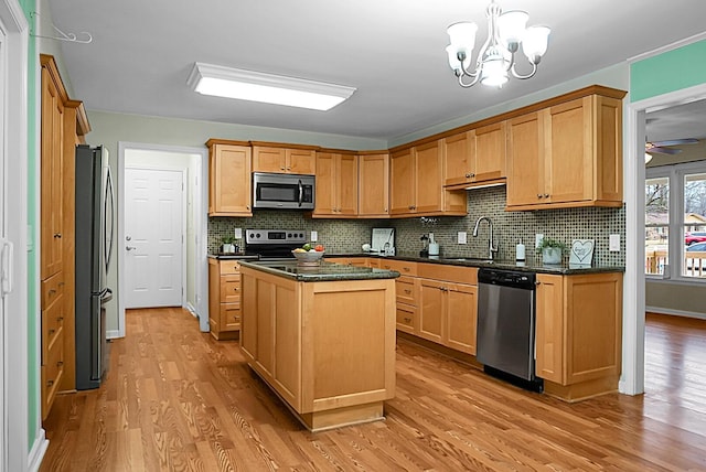 kitchen featuring a center island, stainless steel appliances, dark countertops, a sink, and light wood-type flooring