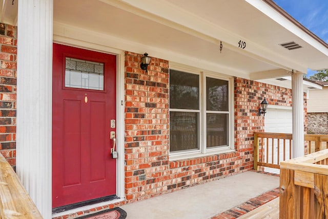 view of exterior entry featuring brick siding and visible vents