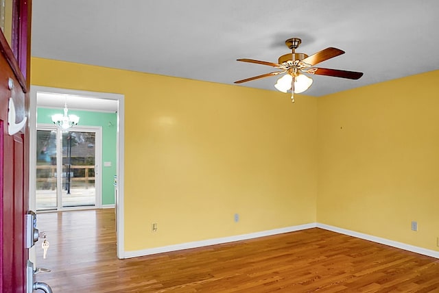 empty room featuring ceiling fan with notable chandelier, wood finished floors, and baseboards