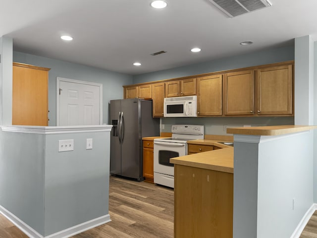 kitchen featuring light wood-style floors, white appliances, visible vents, and a peninsula