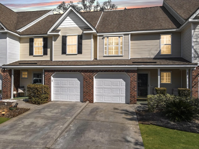 townhome / multi-family property with concrete driveway, brick siding, an attached garage, and a shingled roof