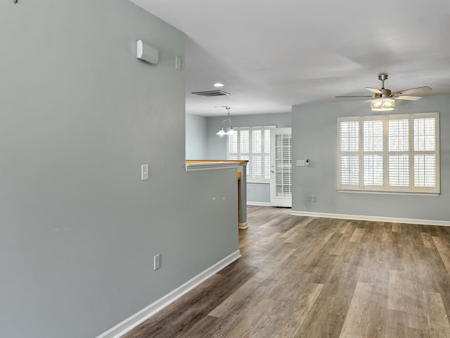 empty room with ceiling fan with notable chandelier, visible vents, baseboards, and wood finished floors