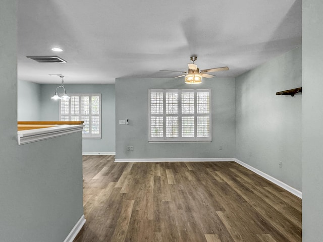 empty room with baseboards, visible vents, dark wood-style flooring, and ceiling fan with notable chandelier