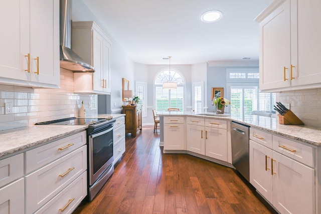 kitchen with wall chimney exhaust hood, stainless steel appliances, white cabinets, and hanging light fixtures