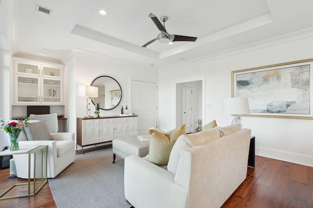 living area with a tray ceiling, wood-type flooring, and visible vents