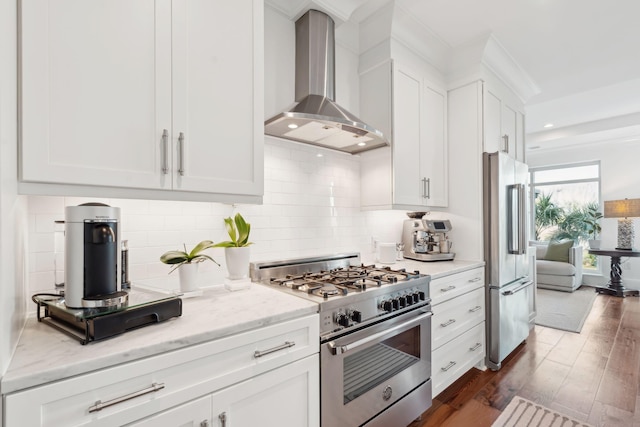 kitchen with white cabinets, premium appliances, wall chimney exhaust hood, light stone counters, and dark wood-style flooring