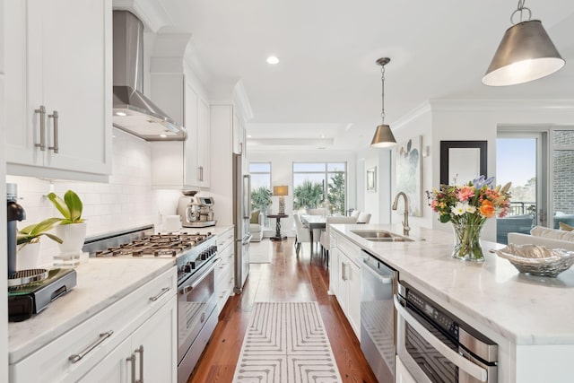 kitchen with stainless steel appliances, dark wood-type flooring, white cabinets, a sink, and wall chimney range hood