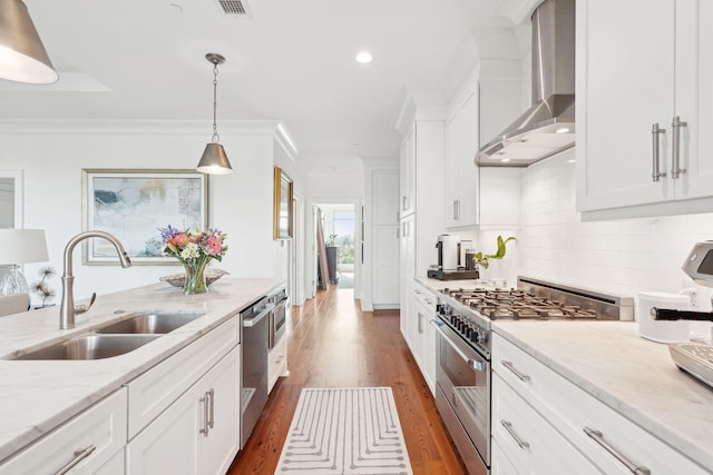 kitchen featuring decorative backsplash, ornamental molding, stainless steel appliances, wall chimney range hood, and a sink