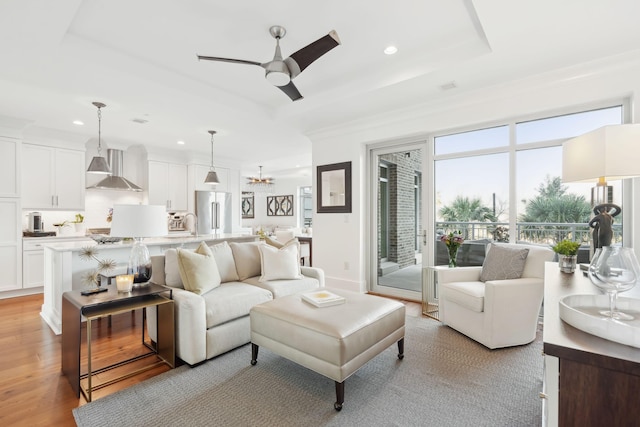 living room with a ceiling fan, a tray ceiling, light wood-style flooring, and recessed lighting