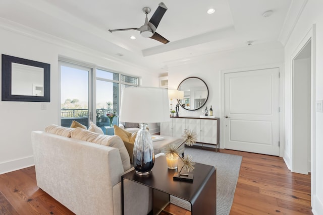 living room with crown molding, wood finished floors, a raised ceiling, and recessed lighting