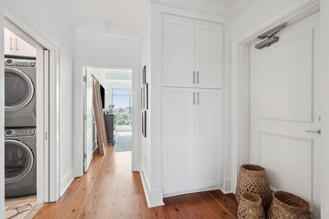 clothes washing area featuring light wood-type flooring, stacked washing maching and dryer, cabinet space, and crown molding