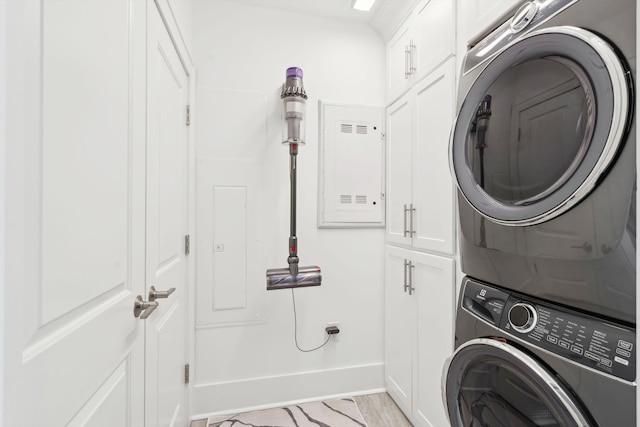 laundry room with stacked washer / dryer, cabinet space, and baseboards