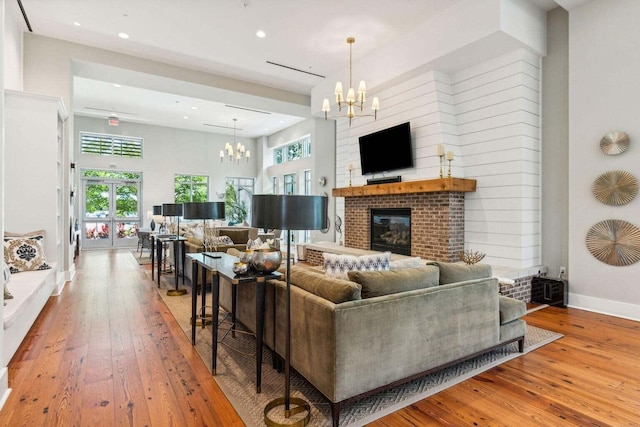 living area featuring hardwood / wood-style flooring, a fireplace, baseboards, french doors, and an inviting chandelier