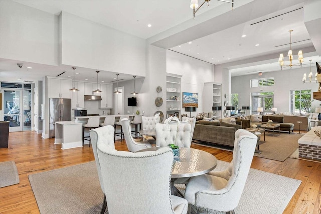 dining area with light wood finished floors, built in features, a high ceiling, a chandelier, and recessed lighting