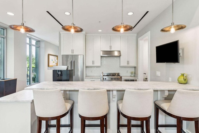 kitchen with white cabinets, decorative backsplash, stove, under cabinet range hood, and high end fridge