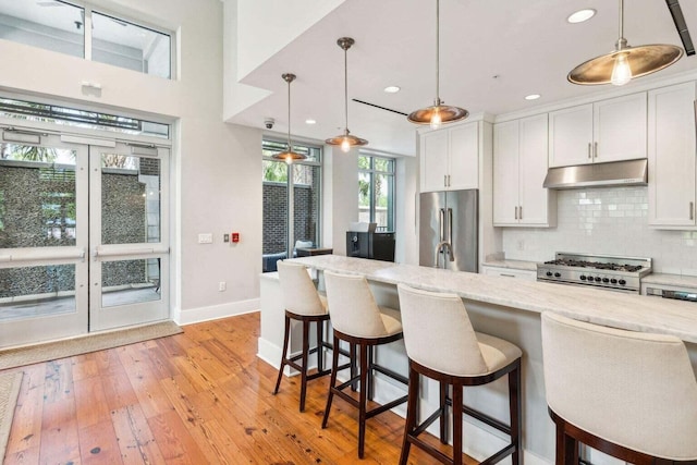 kitchen with tasteful backsplash, range with gas cooktop, high quality fridge, light wood-type flooring, and under cabinet range hood