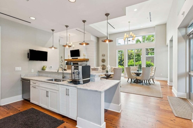 kitchen featuring white cabinets, hardwood / wood-style floors, a peninsula, a sink, and stainless steel dishwasher