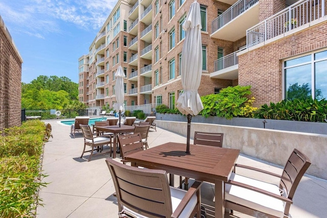 view of patio featuring a community pool, fence, and outdoor dining space