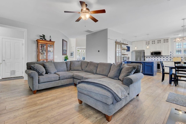 living room featuring ceiling fan with notable chandelier and light hardwood / wood-style floors