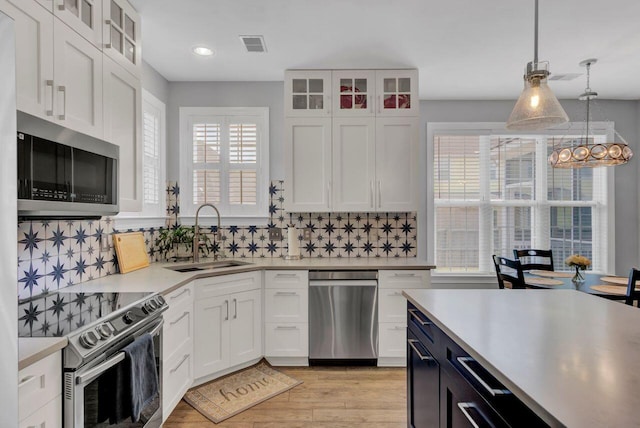 kitchen with white cabinets, sink, hanging light fixtures, decorative backsplash, and stainless steel appliances