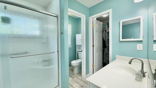 full bathroom with wood finished floors, a shower stall, a spacious closet, vanity, and toilet