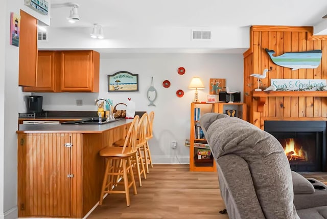 kitchen with a breakfast bar, brown cabinets, a sink, light wood-type flooring, and a peninsula