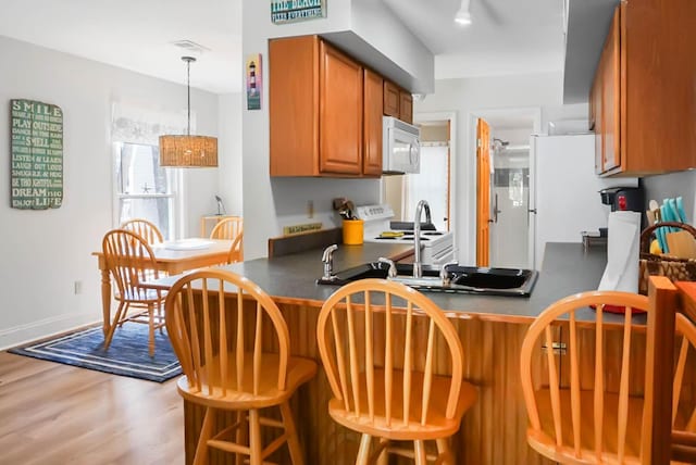 kitchen featuring a peninsula, white appliances, brown cabinets, dark countertops, and a kitchen bar