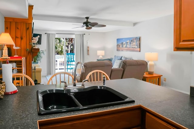 kitchen with brown cabinetry, a ceiling fan, dark countertops, open floor plan, and a sink