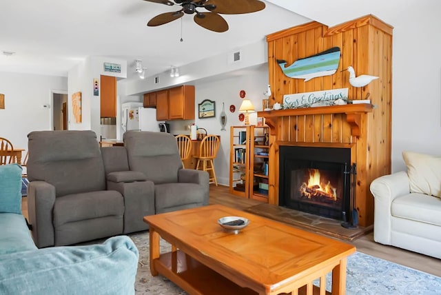 living room featuring a ceiling fan, visible vents, a lit fireplace, and light wood finished floors