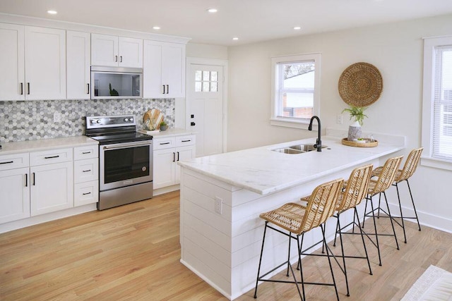 kitchen featuring a sink, light wood-style flooring, stainless steel appliances, tasteful backsplash, and a kitchen bar